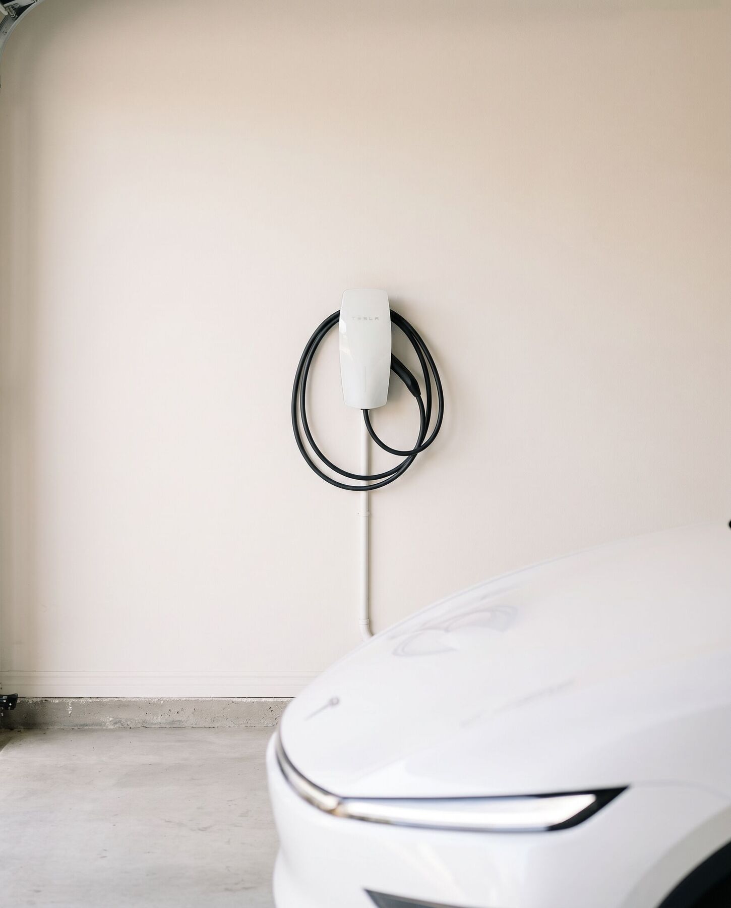 A white Tesla Gen 3 Wall Connector mounted on a garage wall beside a 2026 Model Y